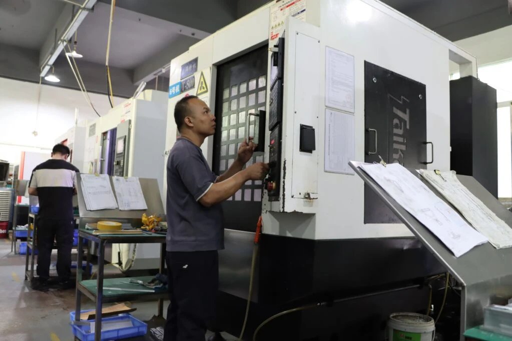Machine operator working at a CNC machining center beside production drawings on the factory floor