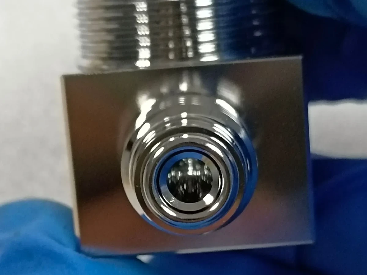 Electropolished metal fitting with a reflective square body, central bore and threaded boss