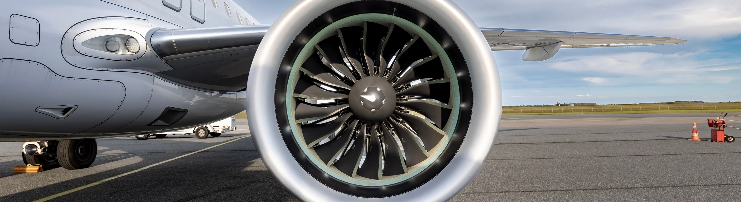 Jet engine fan blades and intake beside an aircraft fuselage on an airport apron