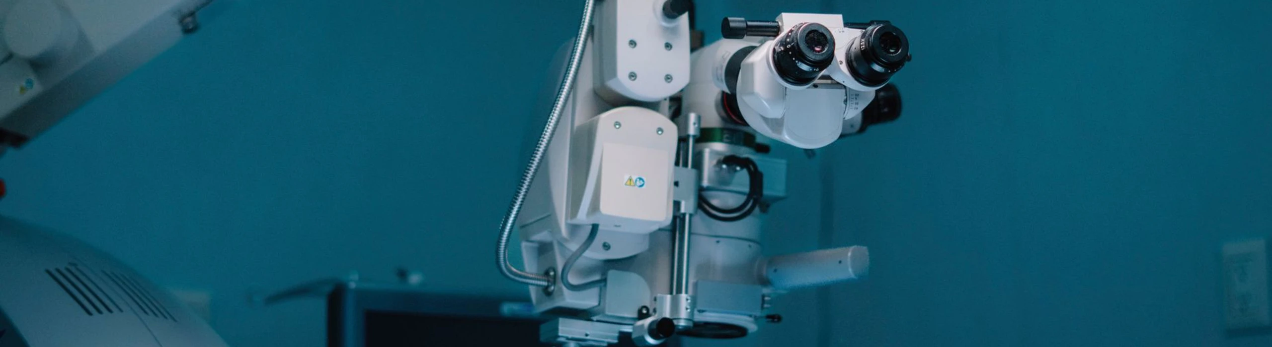 Surgical microscope with binocular eyepieces in a teal-lit medical room