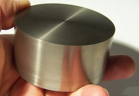 A short titanium cylinder held in a hand, with a flat circular end and straight sides