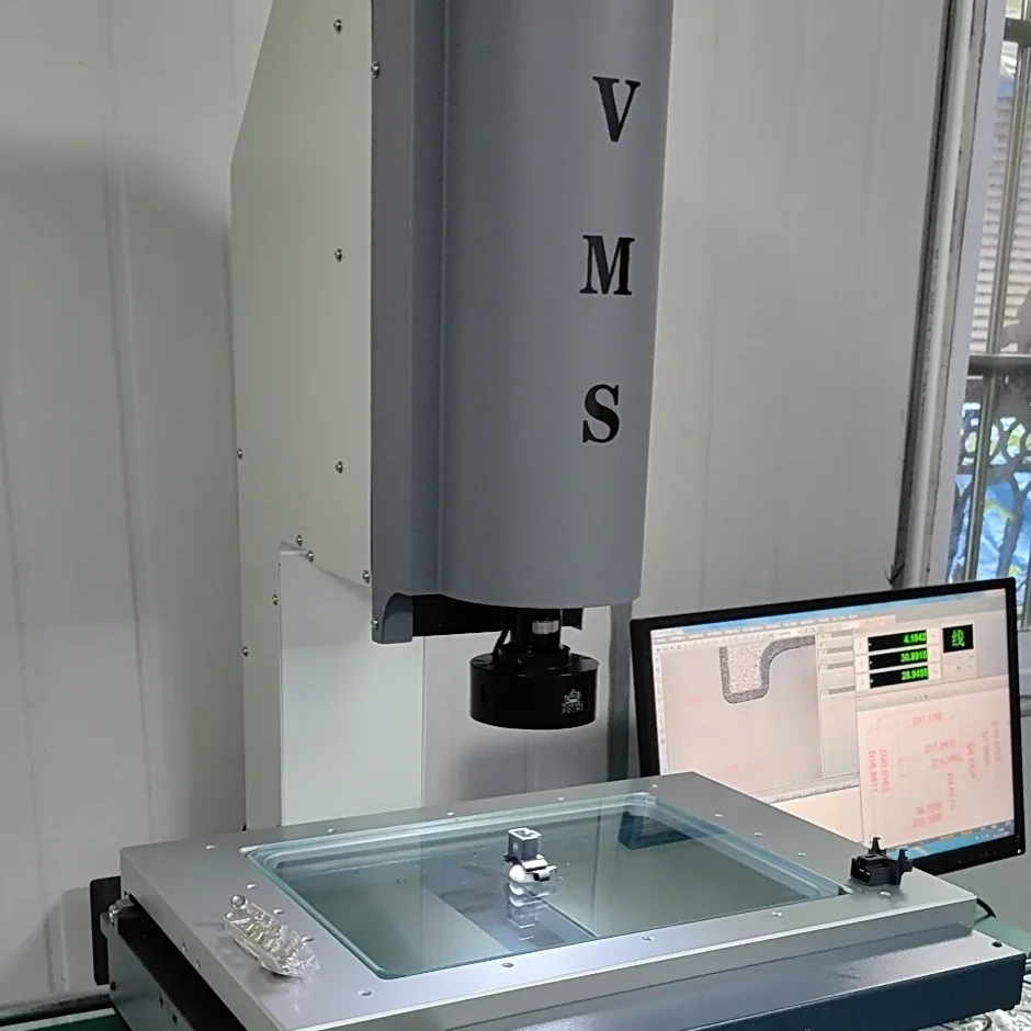 Video measuring system inspecting a small metal component on a glass stage beside a measurement display