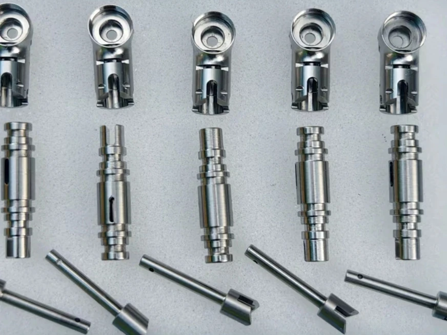 Rows of small metal instrument components with circular recesses, stepped shafts and cross-holes