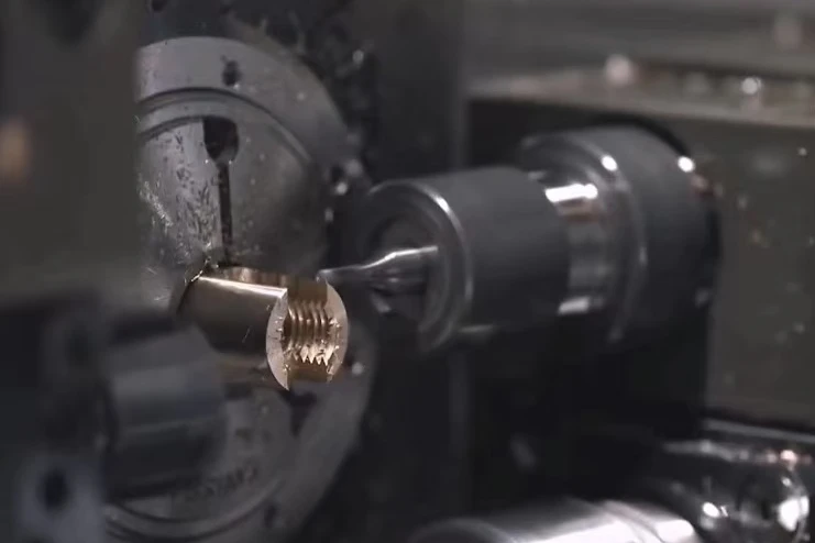 Swiss machining tooling working on a small threaded metal component held inside the machine