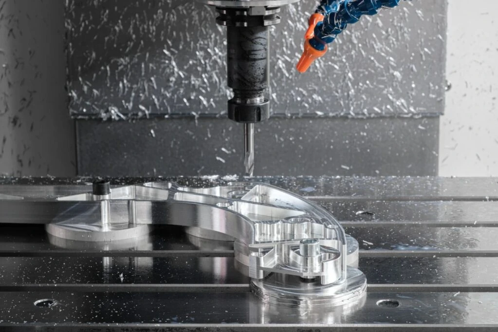 CNC milling spindle above a contoured metal component clamped to a machine table, with milled pockets and bores