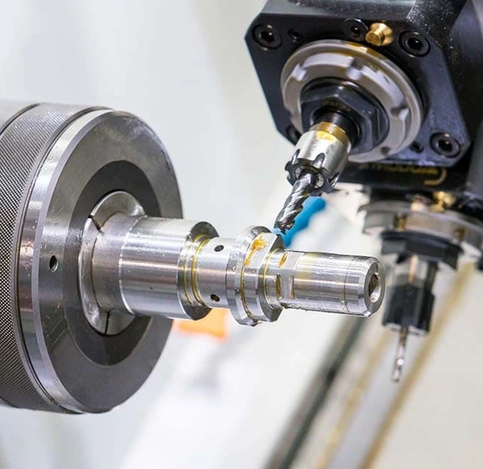 A live milling tool machining a stepped metal shaft clamped in a lathe chuck