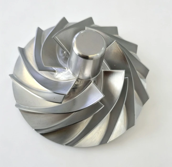A machined metal impeller with curved blades and a cylindrical center hub