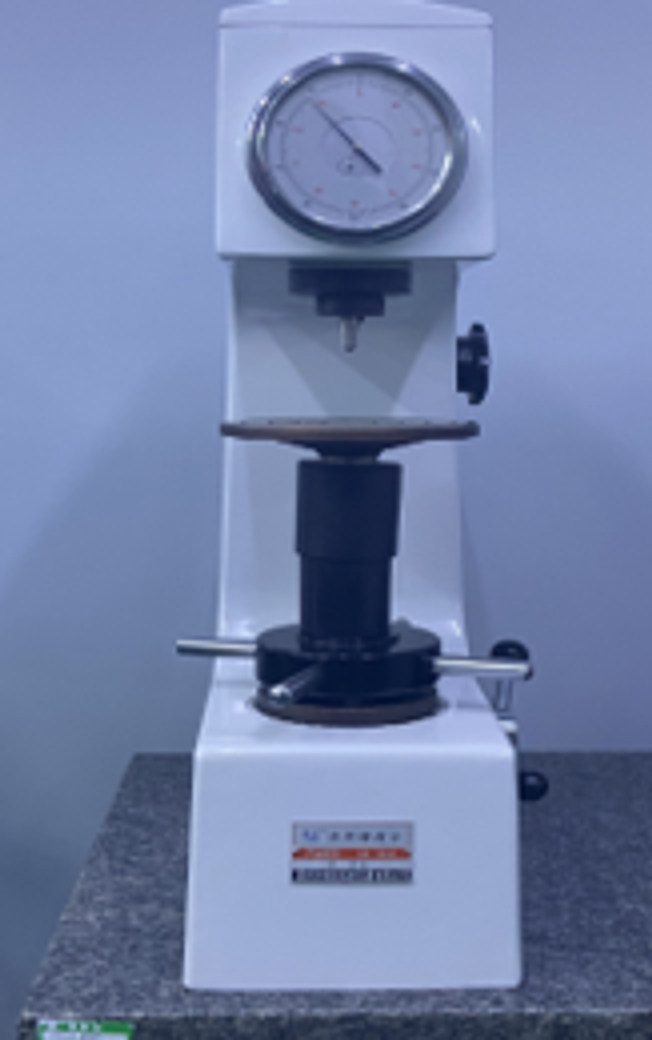 Rockwell hardness tester with analog dial, loading anvil and handwheel on a granite bench