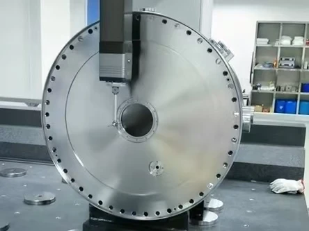 Coordinate measuring probe inspecting a large circular metal plate with a central bore and perimeter holes